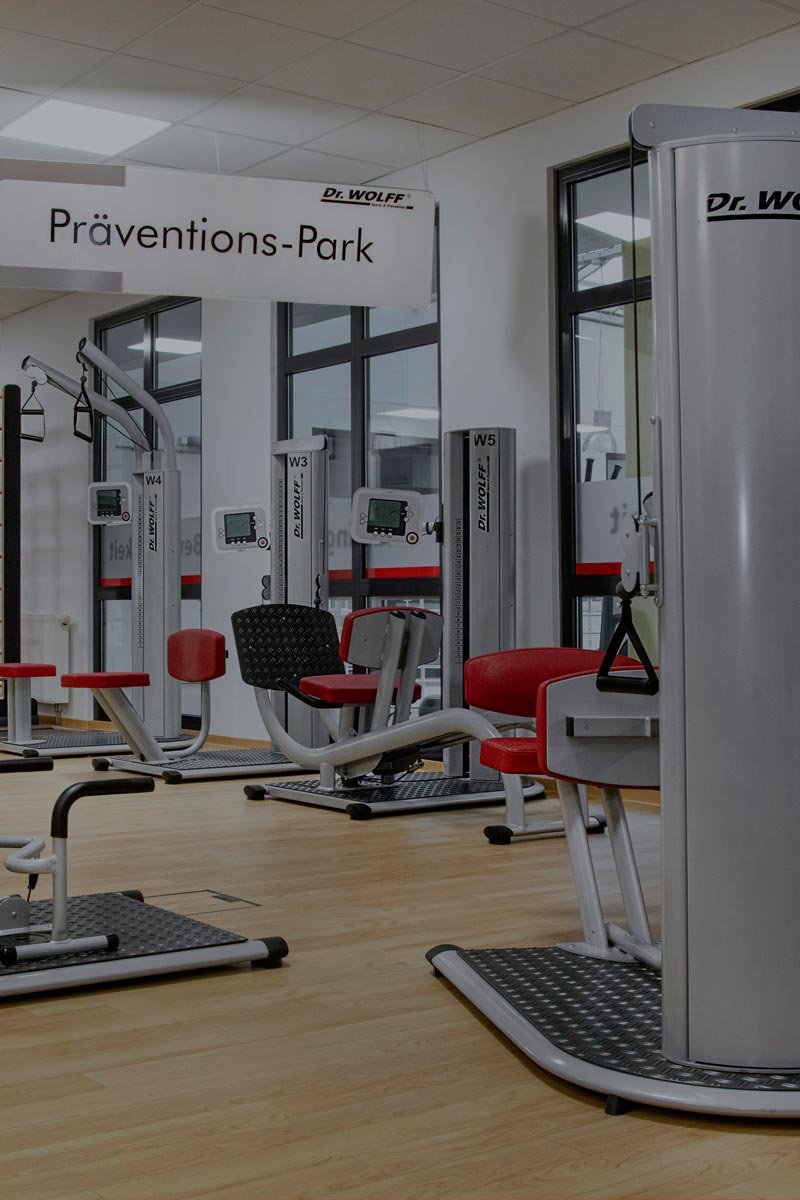 Fitnessstudio mit roten Polstern und modernen Geräten, helles Holz und Glaswände im Hintergrund.